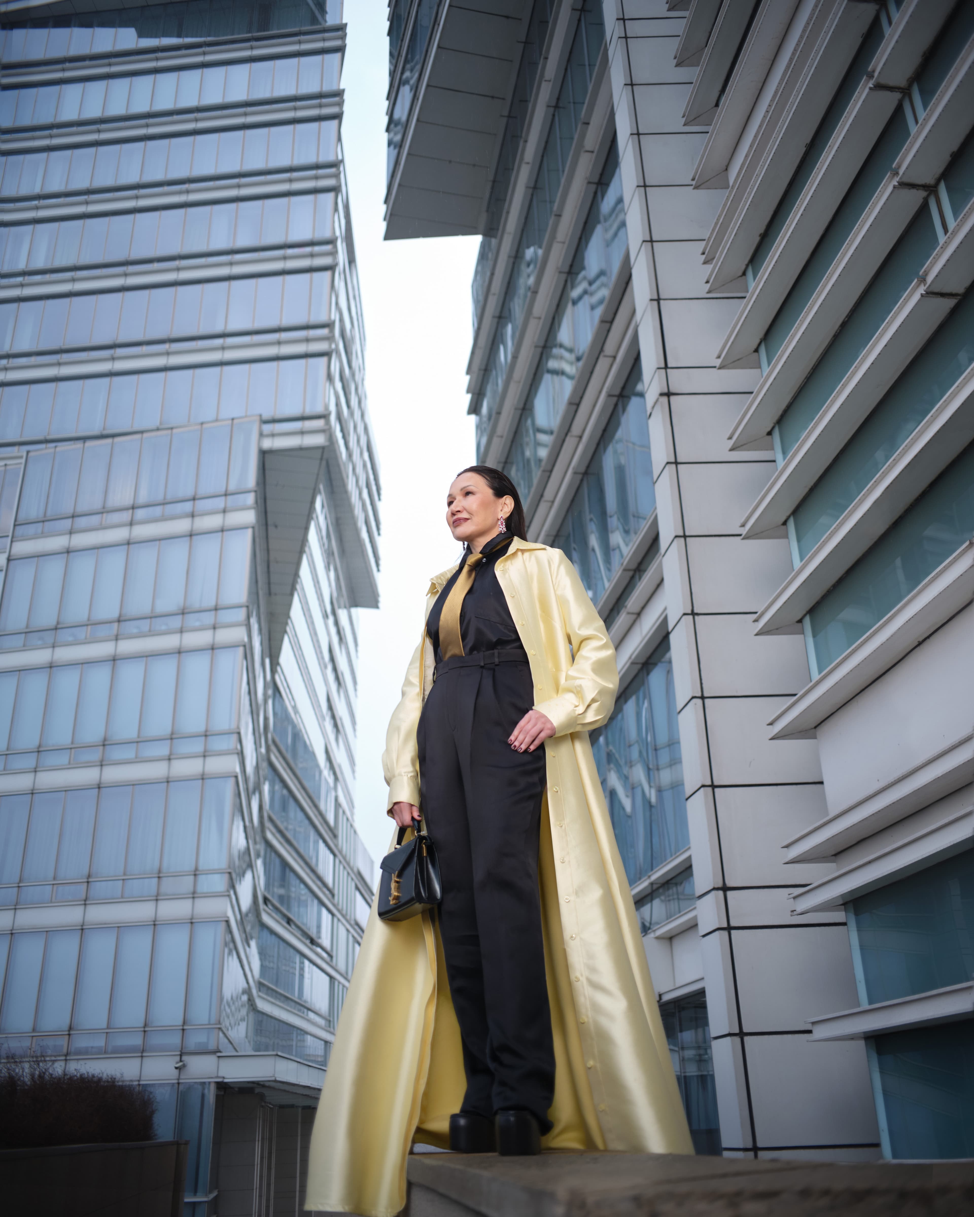 Атласное платье-рубашка, надетое как пальто Greta Constantine
Брюки и сумка Saint Laurent 
Рубашка Loewe 
Галстук Zegna
Туфли Gucci
Серьги Chopard High Jewellery